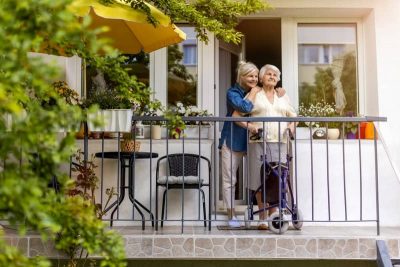 Une femme âgée avec un déambulateur admire son jardin depuis son balcon