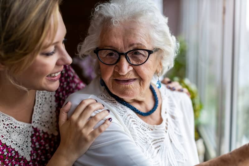 Une femme âgée sourit à sa fille, qui la tient par les épaules avec tendresse