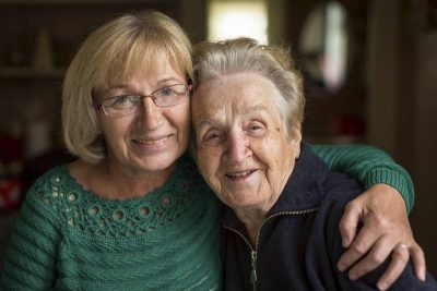 Une femme âgée et sa fille se tiennent par l'épaule en souriant